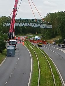 The photo shows the bridge being lifted by the crane and being rotated through 90 degrees so that it crosses the Spine Road