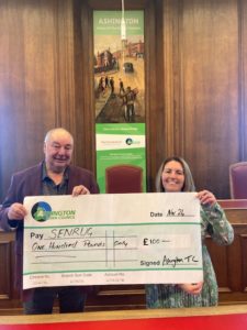 Dennis Fancett and Cllr Caroline Ball jointly holding a large presentation cheque in the Ashington Council Chamber