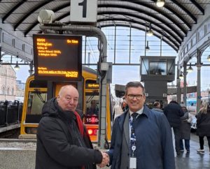 Dennis Fancett and Northern;s Regional Director Jason Wade shaking hands in front of a train information display showing Ashington